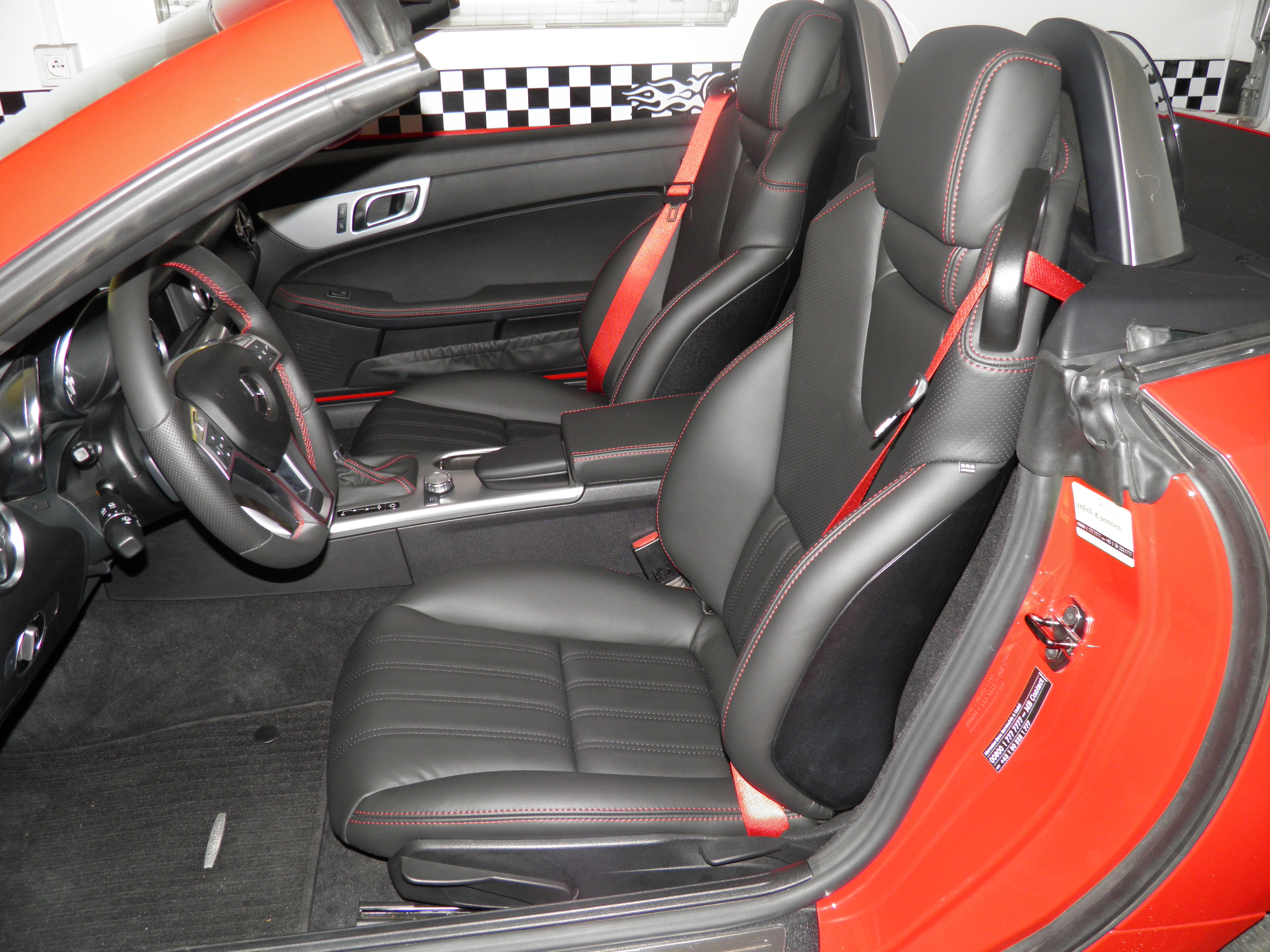 Czerwony kabriolet z czarną skórzaną tapicerką, czerwoną nicią i pasami. Wnętrze po renowacji, widoczne fotele, kierownica i deska rozdzielcza.