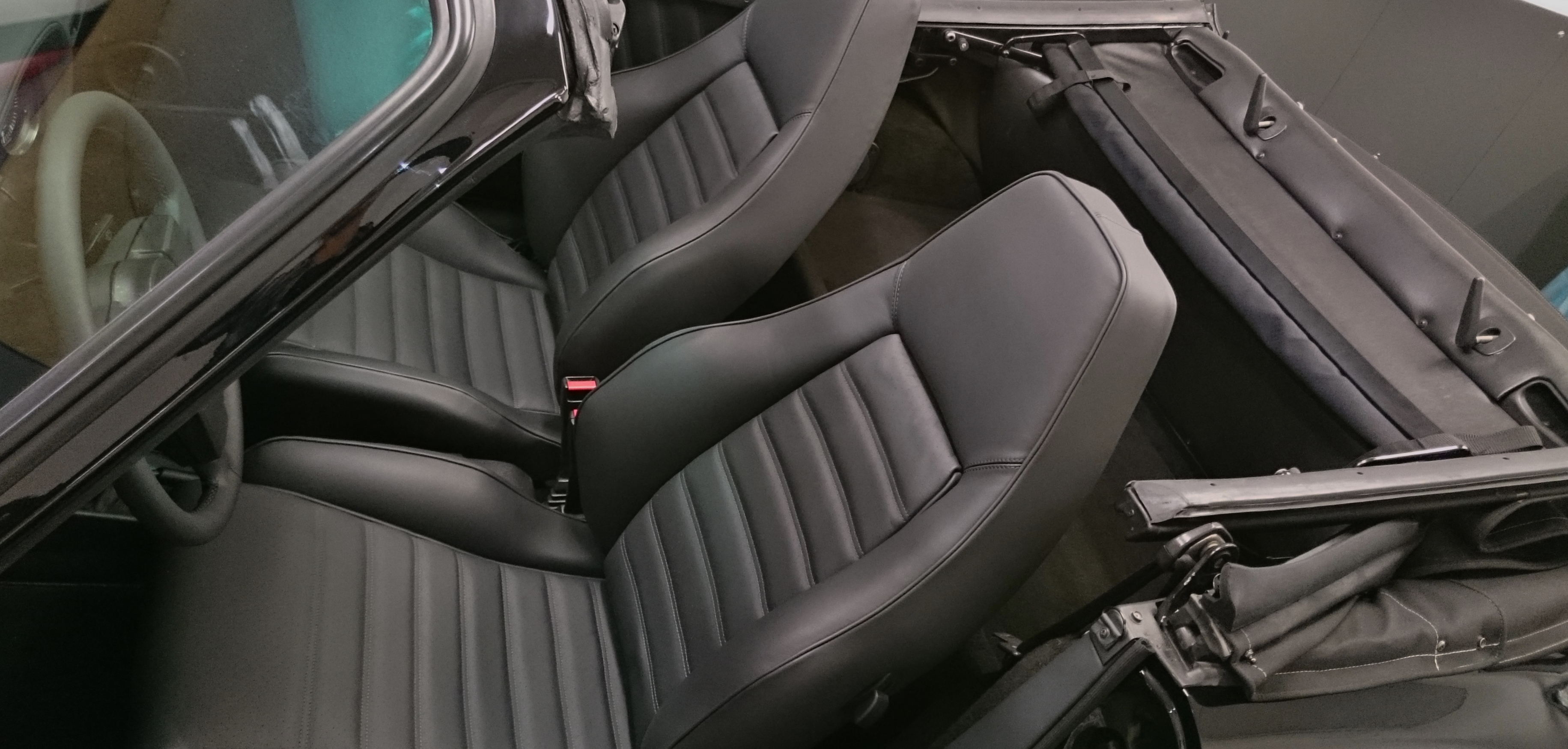 Czarne, skórzane fotele z pionowymi przeszyciami w kabriolecie, widoczne z góry. Fragment kierownicy i mechanizm składania dachu.