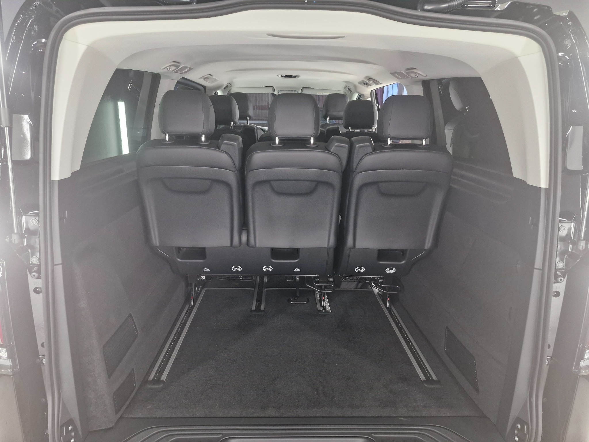 Wnętrze luksusowego busa z trzema rzędami czarnych skórzanych foteli, widok z tyłu pojazdu, ukazujący przestronność i komfort podróży.