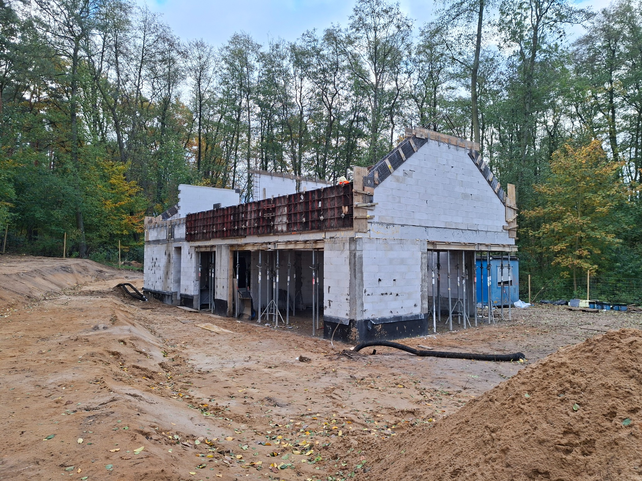 Wznoszenie ścian domu z betonu komórkowego. Widoczne szalunki i podpory. W tle drzewa i usypana ziemia.