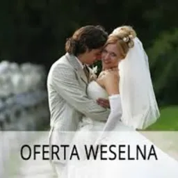 Para młoda w objęciach na tle zieleni, oferta weselna. Panna młoda w białej sukni i welonie, pan młody w jasnym garniturze. Romantyczna atmosfera.