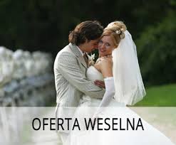 Para młoda w objęciach na tle zieleni, oferta weselna. Panna młoda w białej sukni i welonie, pan młody w jasnym garniturze. Romantyczna atmosfera.