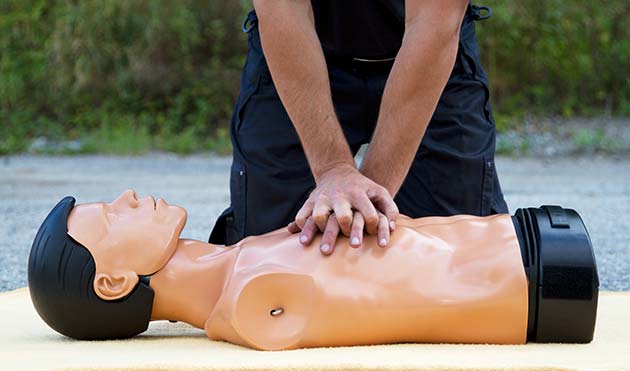 Instruktor wykonuje resuscytację krążeniowo-oddechową na manekinie podczas kursu pierwszej pomocy, widoczne ręce instruktora i tors manekina.