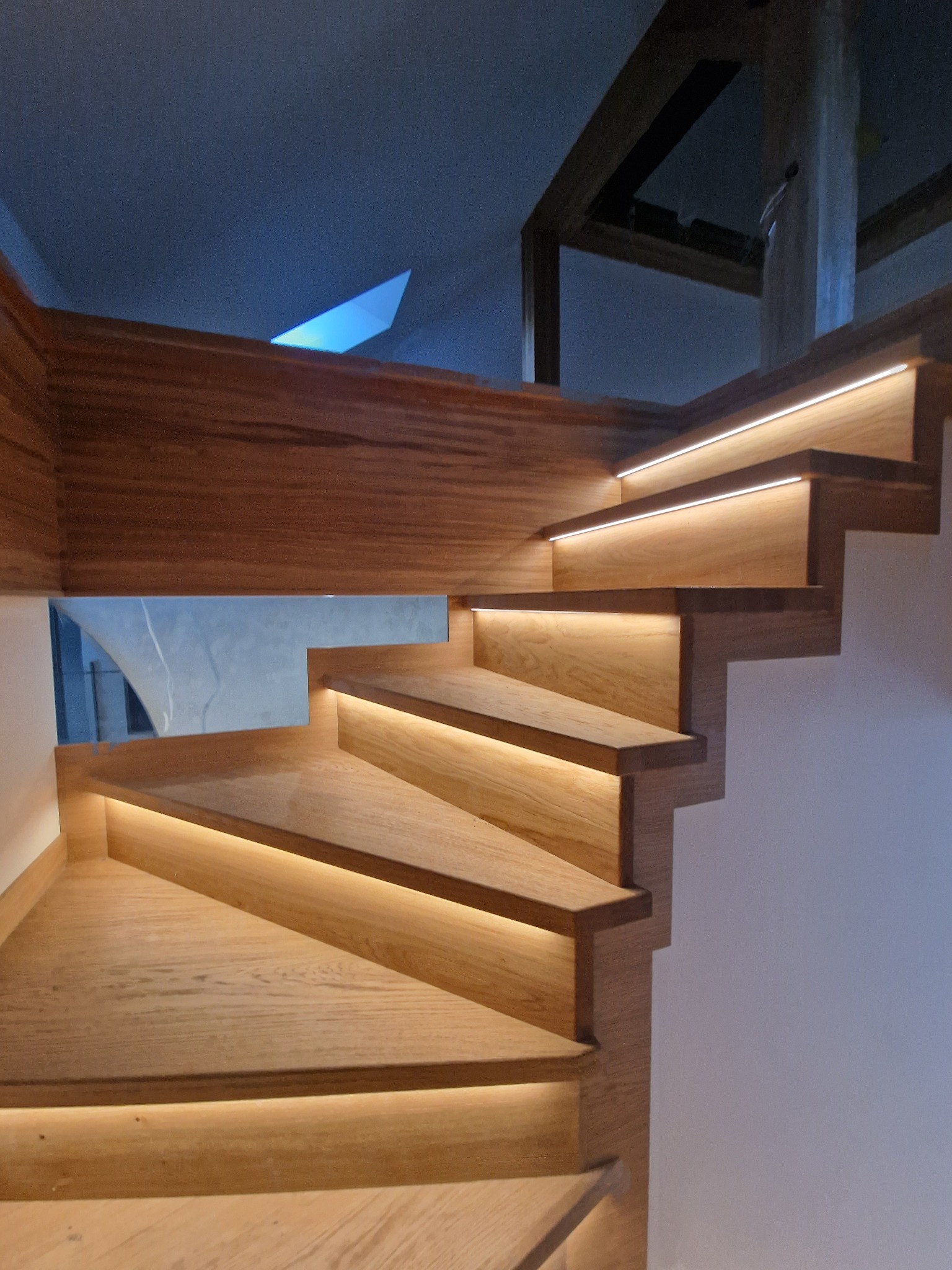 Drewniane schody z subtelnym oświetleniem LED pod stopniami, widok z dołu, nowoczesny design, ciepłe światło, minimalistyczne wykończenie.