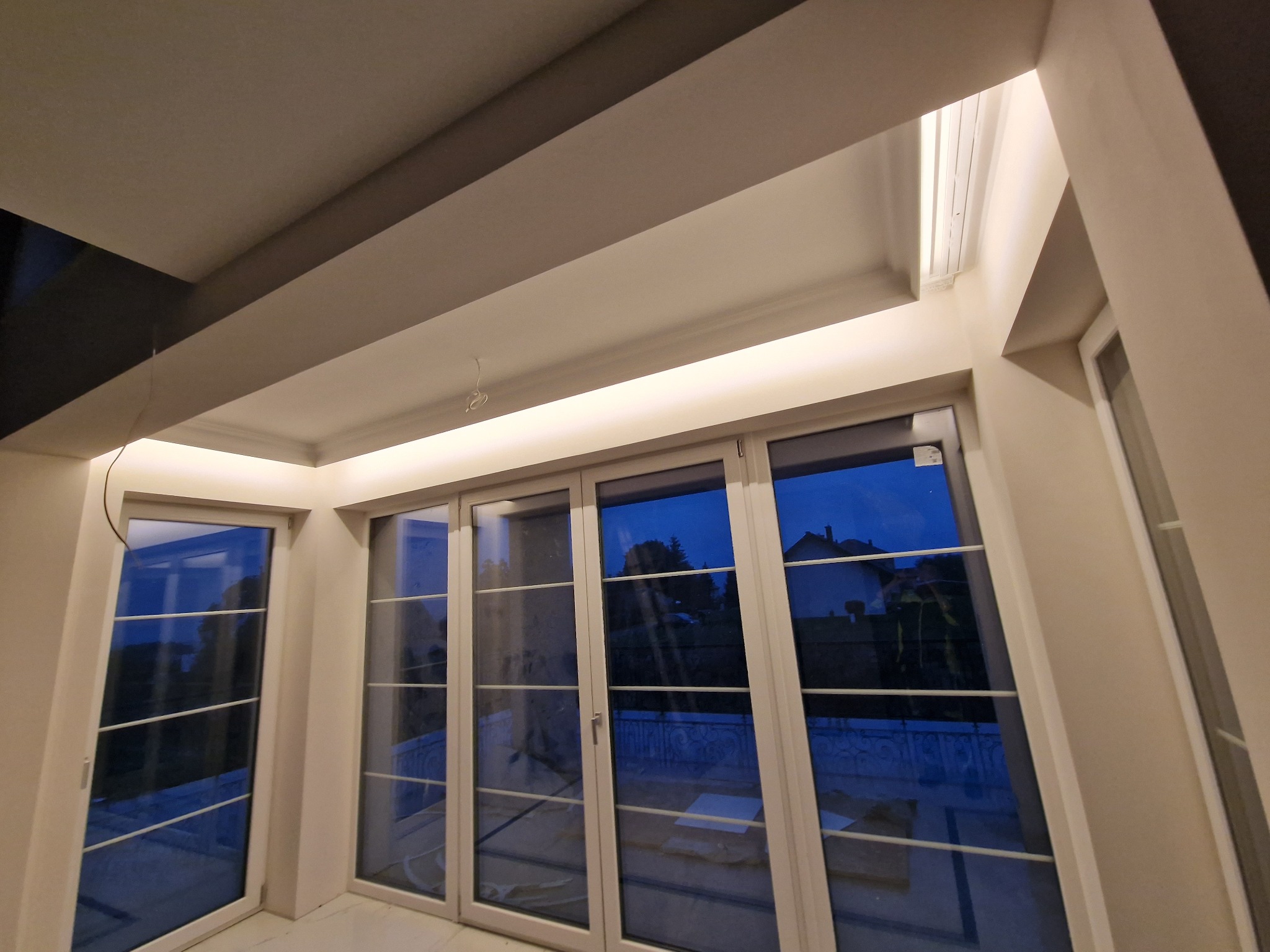 Nowoczesne oświetlenie LED w podwieszanym suficie, widoczne okna z odbiciem nocnego krajobrazu. Minimalistyczny design, ciepłe światło.