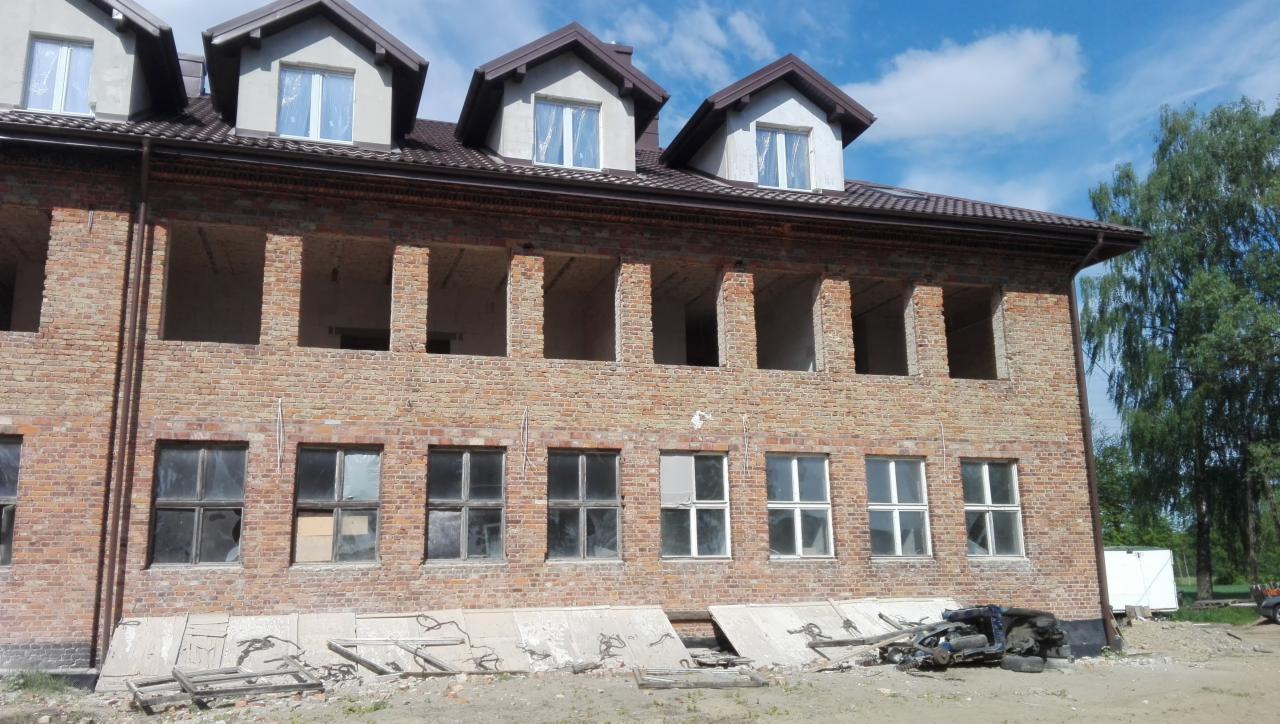 Dwupiętrowy budynek z czerwonej cegły w trakcie budowy lub remontu, z niezabudowanymi otworami okiennymi na drugim piętrze i częściowo zamontowanymi oknami na pierwszym, z gruzem i elementami...