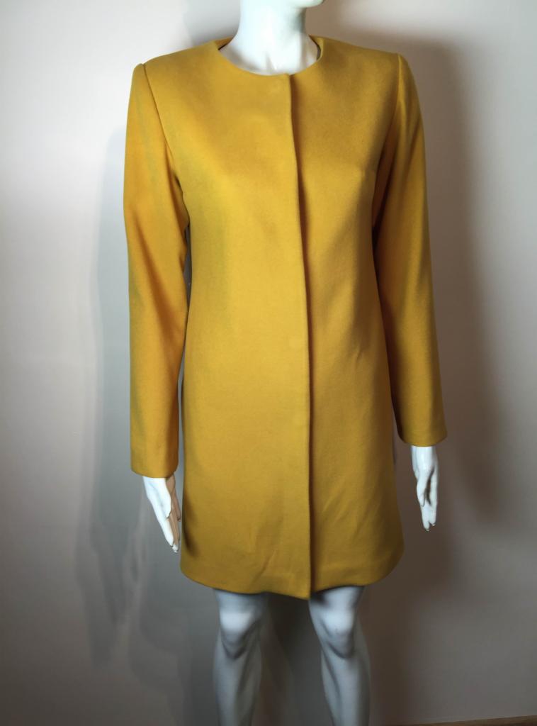 Musztardowy płaszcz damski o prostym kroju, zapinany na zatrzaski, prezentowany na manekinie w neutralnym otoczeniu.