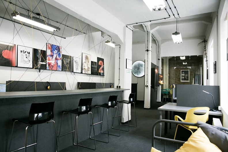 Nowoczesne wirtualne biuro z czarnymi krzesłami barowymi, designerskimi plakatami i kreatywną instalacją z linek na ścianie. Przestrzeń biurowa w stylu loft.