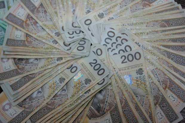 Stos banknotów 200 zł ułożonych wachlarzowo, z widocznymi detalami nominałów i hologramami. Jasne oświetlenie podkreśla fakturę papieru.