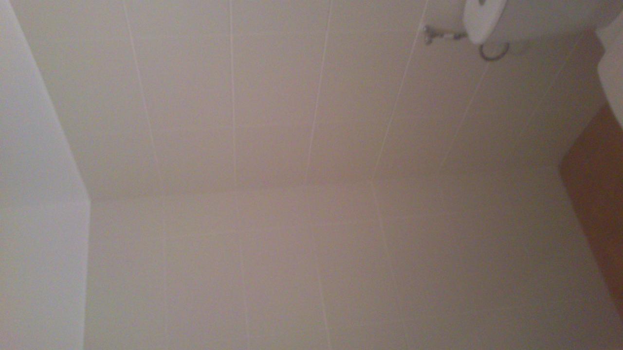 Jasne, świeżo położone płytki w łazience, widok z dołu, z fragmentem bojlera i szafki. Minimalistyczny design, neutralne kolory.