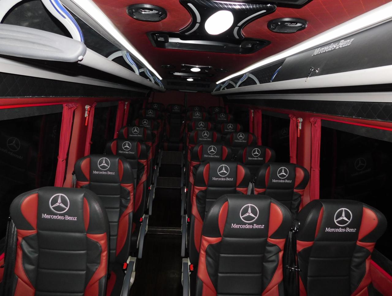 Wnętrze luksusowego autobusu Mercedes-Benz z czerwono-czarnymi skórzanymi siedzeniami, gotowego do wynajmu w Warszawie. Widoczne logo Mercedes-Benz na każdym siedzeniu.