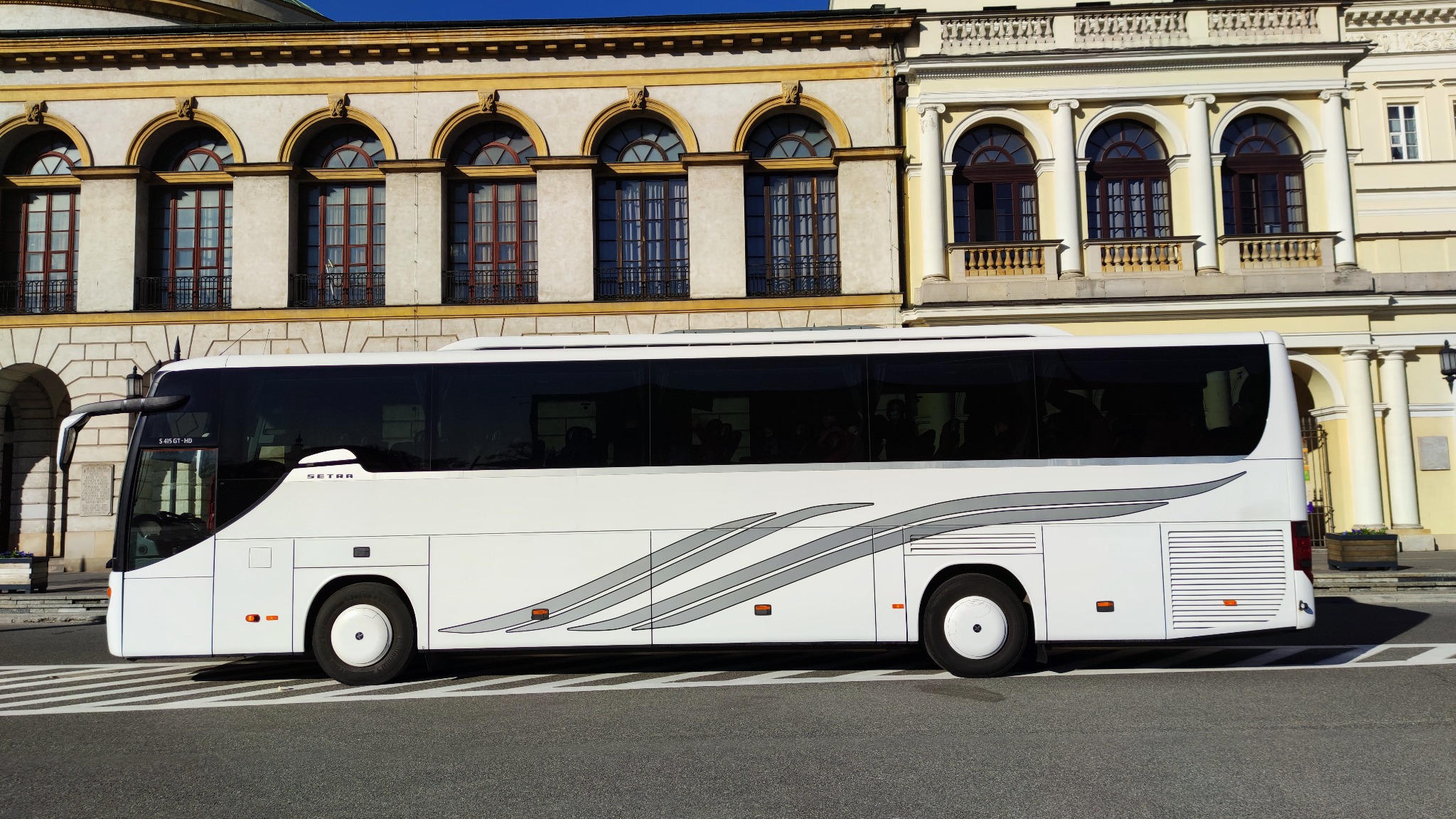 Biały autokar Setra na tle klasycystycznej architektury miejskiej, widok z boku, pasy na karoserii.