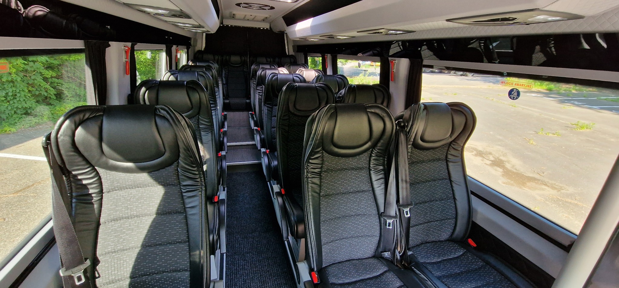 Wnętrze autobusu z rzędami czarnych, skórzanych foteli z pasami bezpieczeństwa, widok z przodu pojazdu.