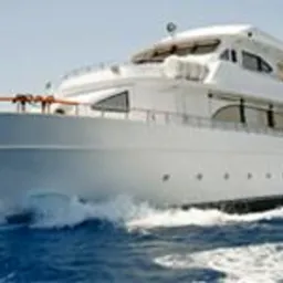 Biały jacht motorowy płynie po błękitnych wodach, tworząc pianę. Widok z boku, jasne oświetlenie, dynamiczne ujęcie podkreślające ruch i luksusowy charakter jednostki.