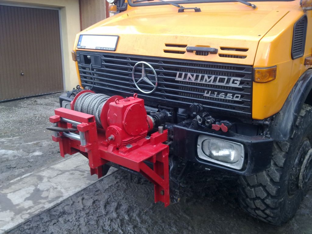 Żółty Unimog U1650 z czerwoną wyciągarką linową zamontowaną z przodu, widok z bliska, zarys opony w błocie.