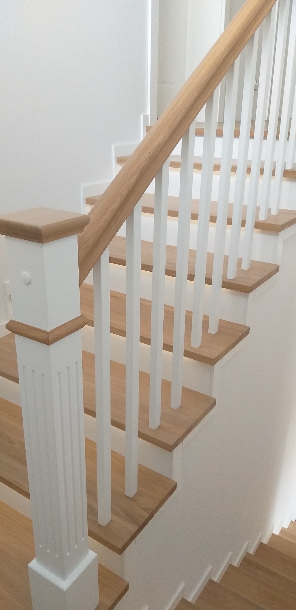 Jasne drewniane schody z białymi, pionowymi balustradami i drewnianą poręczą, widok z dołu, minimalistyczny design.