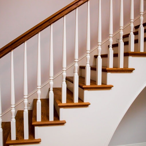 Klasyczne schody z jasnego drewna i białymi balustradami, widok z dołu, ukazujący eleganckie wykończenie i detale.