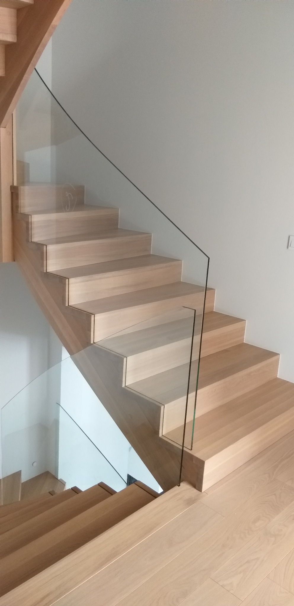 Jasne, drewniane schody z minimalistyczną szklaną balustradą, widok z dołu, nowoczesny design.