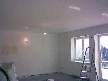 Wnętrze pokoju po remoncie: białe ściany, okna z widokiem na zieleń, drabina oparta o ścianę. Na ścianie widoczne ślady po malowaniu.