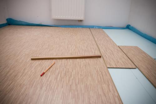 Układanie paneli podłogowych w jasnym wnętrzu, widoczne narzędzia: listwa i ołówek. Częściowo ułożona podłoga na podkładzie izolacyjnym.