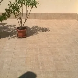 Wyłożony jasnymi płytkami taras w budynku wielorodzinnym z dwoma donicami z roślinami, widok z góry.