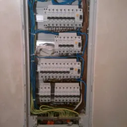 Rozdzielnica elektryczna z licznymi zabezpieczeniami i okablowaniem w Nowej Kuźnicy. Widoczne kable w kolorach niebieskim, brązowym i żółto-zielonym.