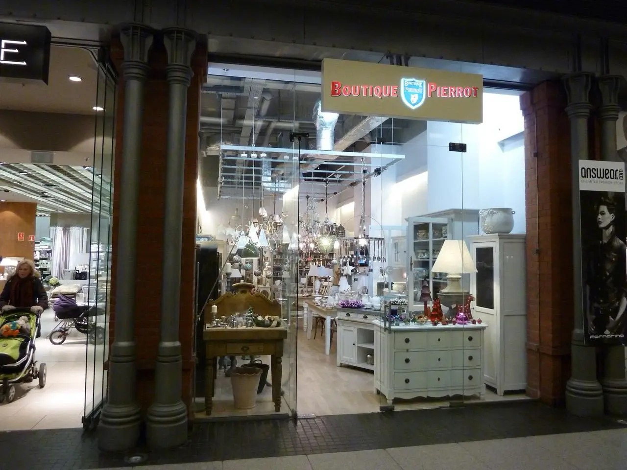 Eleganckie wejście do butiku 'Boutique Pierrot' z przeszkloną fasadą, kolumnami i widocznym wnętrzem pełnym mebli i dekoracji w jasnych barwach.