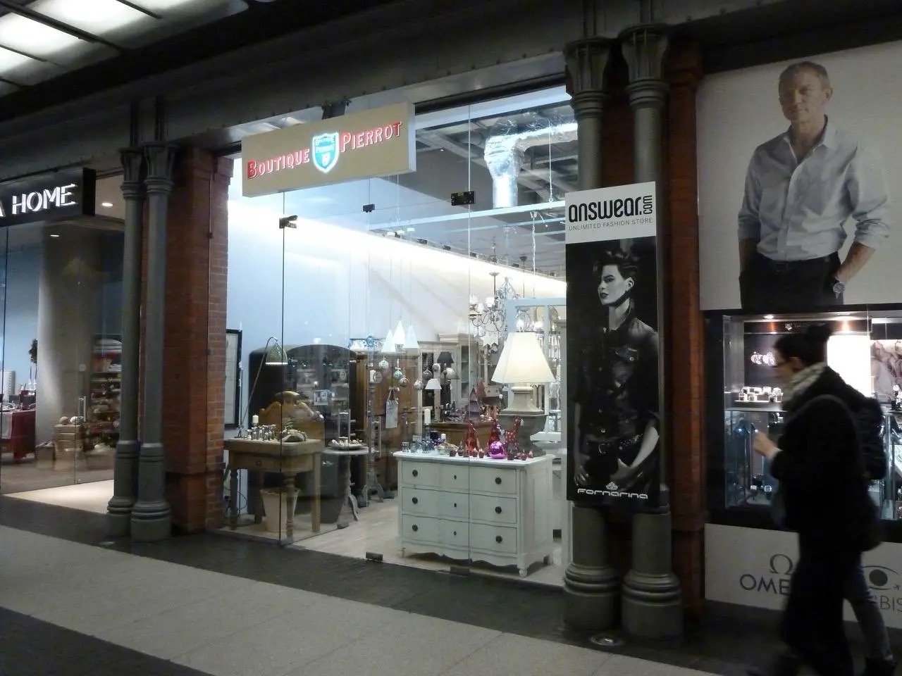 Elegancka witryna butiku 'Boutique Pierrot' z ekspozycją mebli i dekoracji, widoczna przez szklaną fasadę. W tle reklama Answer.com i Omega Bis.