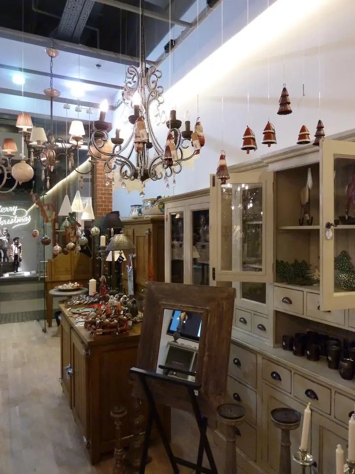 Wnętrze sklepu z antykami: drewniane meble, żyrandole w stylu retro, dekoracje świąteczne. Widoczny fragment ekspozycji z lustrem w drewnianej ramie i szafki z ozdobami.