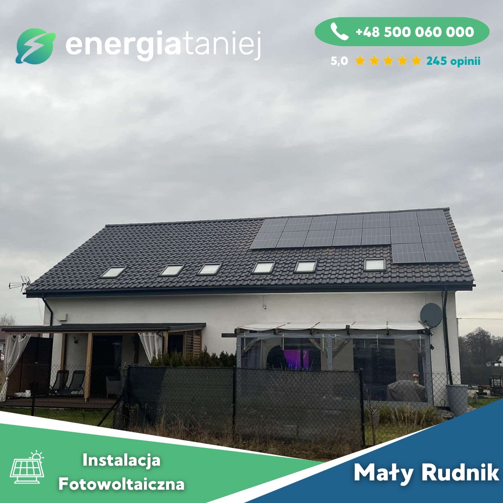 Dom jednorodzinny z częściowo zainstalowanymi panelami słonecznymi na dachu pokrytym czarną dachówką, widoczne okna dachowe i antena. Na pierwszym planie czarne ogrodzenie siatkowe.