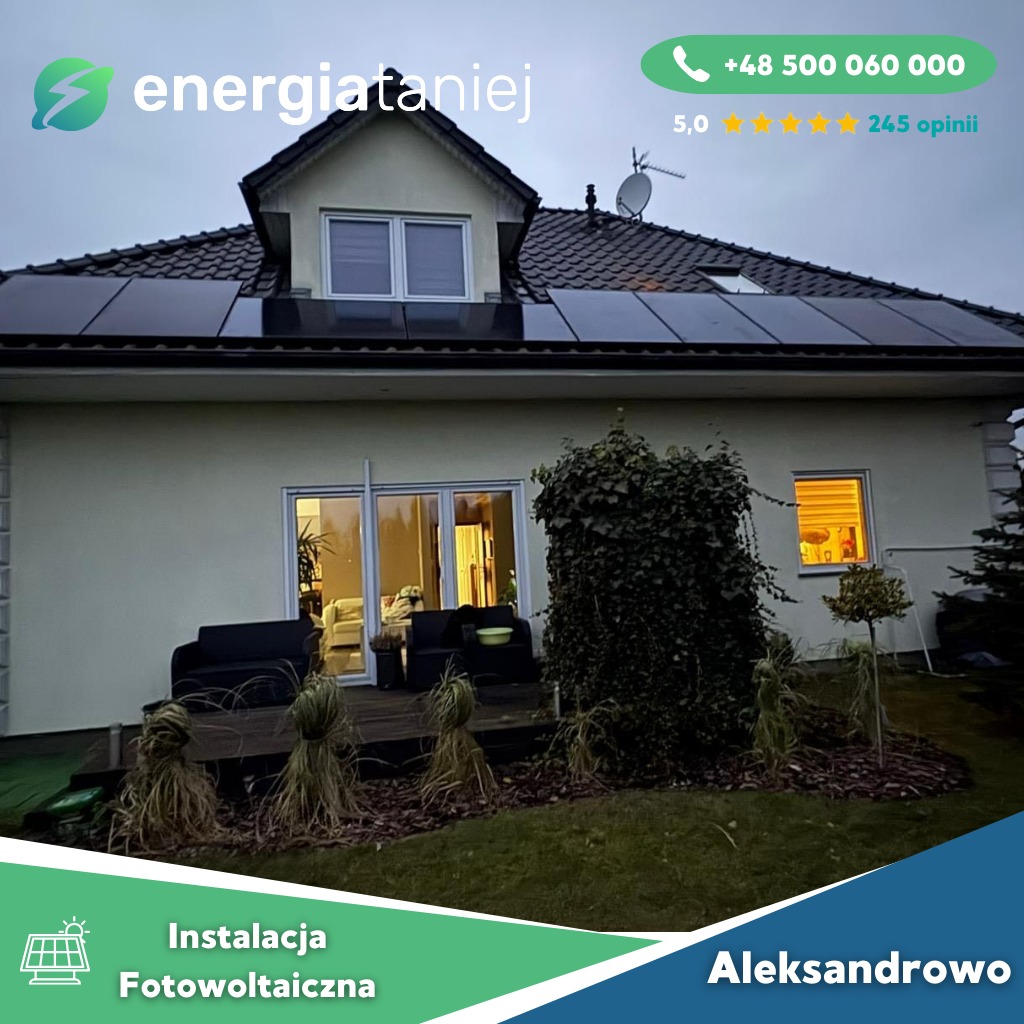 Dom jednorodzinny z zainstalowanymi panelami słonecznymi na dachu, widok z ogrodu, z podświetlonym oknem po prawej stronie i tarasem z meblami ogrodowymi.