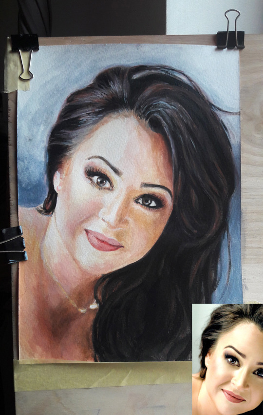 Portret kobiety z ciemnymi włosami, namalowany akwarelami, przypięty klamrami do deski, obok widoczna fotografia referencyjna.