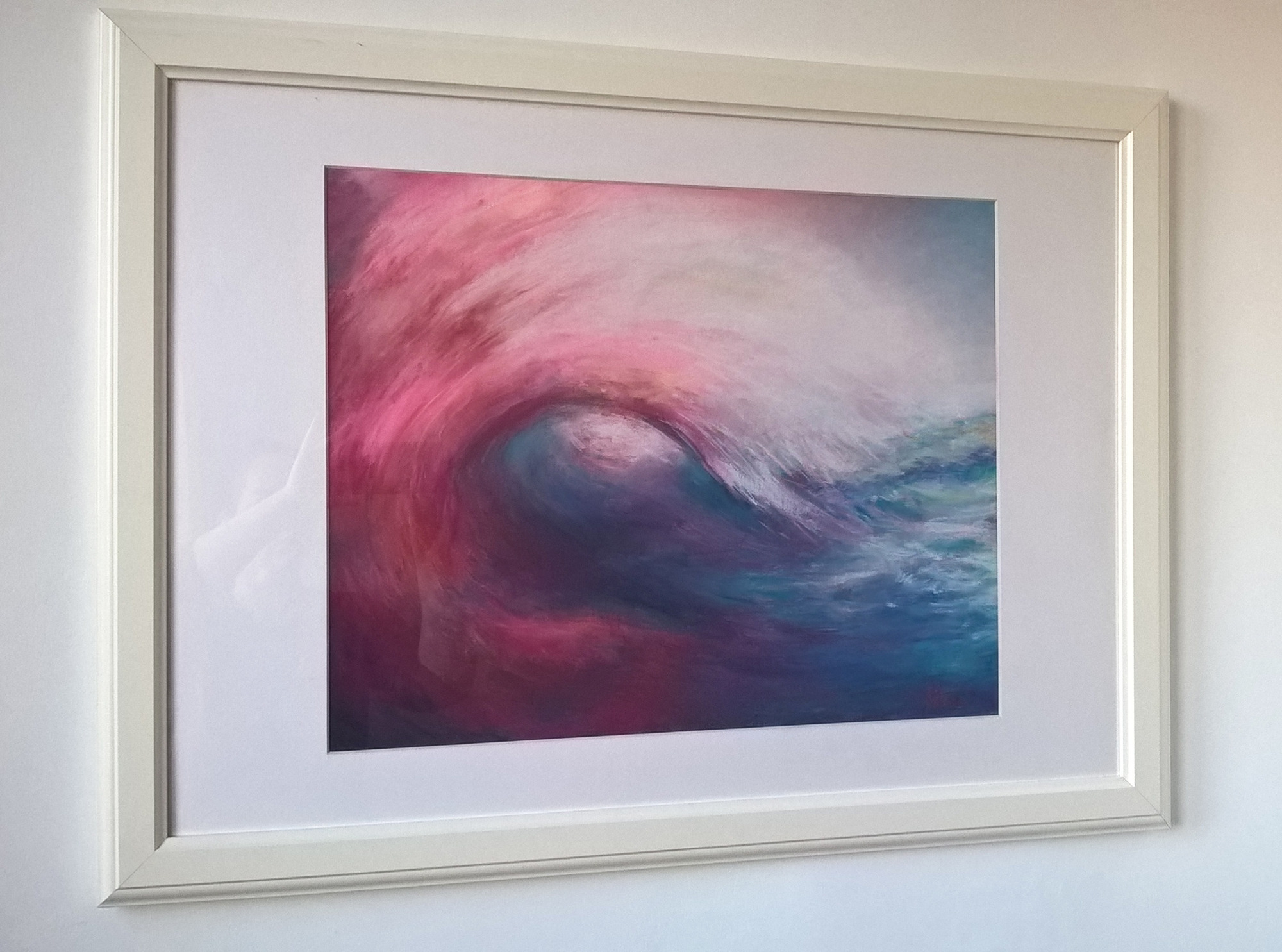 Abstrakcyjne malowidło przedstawiające falę w odcieniach różu, fioletu i błękitu, oprawione w białą ramę i zawieszone na jasnej ścianie.