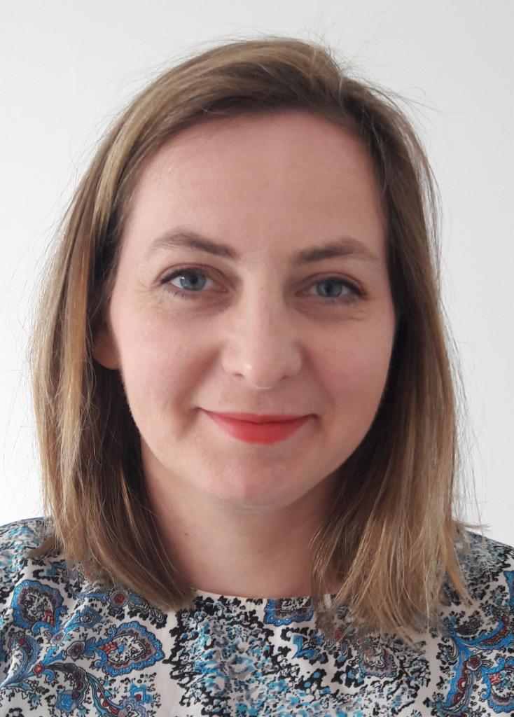 Portret kobiety z niebieskimi oczami i pomalowanymi ustami, ubranej w bluzkę we wzory. Jasne tło, naturalne światło.