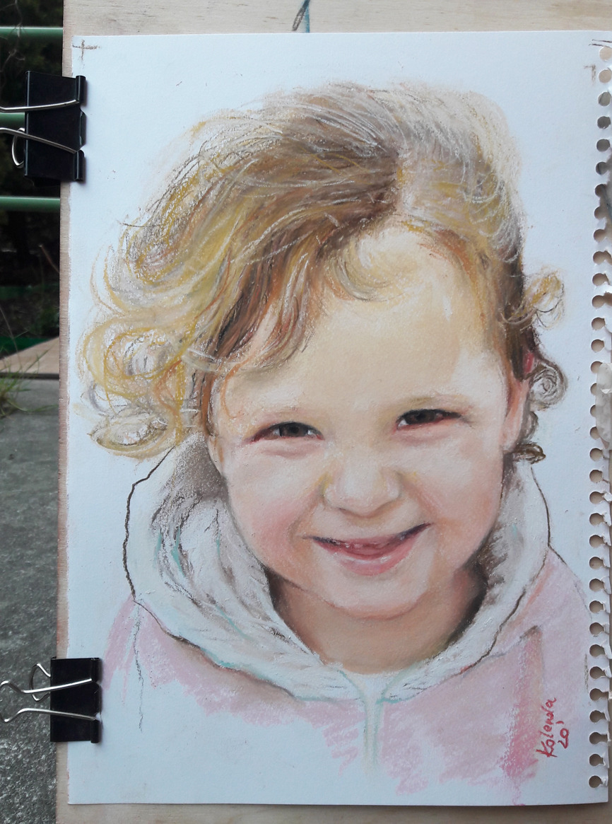 Portret dziewczynki z blond lokami, wykonany pastelami na papierze, z widocznym podpisem artysty w prawym dolnym rogu i spinaczami biurowymi przytrzymującymi kartkę.