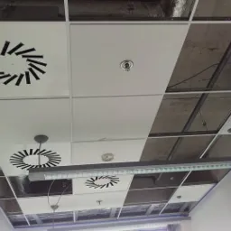 Sufit podwieszany kasetonowy z kratką wentylacyjną i oświetleniem LED w biurze, widok od dołu, część kasetonów zdjęta, odsłaniając instalacje.