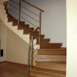 Drewniane schody z metalową balustradą, jasne drewno stopni i podłogi, kremowe ściany, widok z dołu