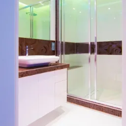 Nowoczesna łazienka z kabiną prysznicową ze szklanymi drzwiami przesuwnymi, umywalką nablatową na brązowym blacie i białymi szafkami, oświetlona kolorowym światłem LED.