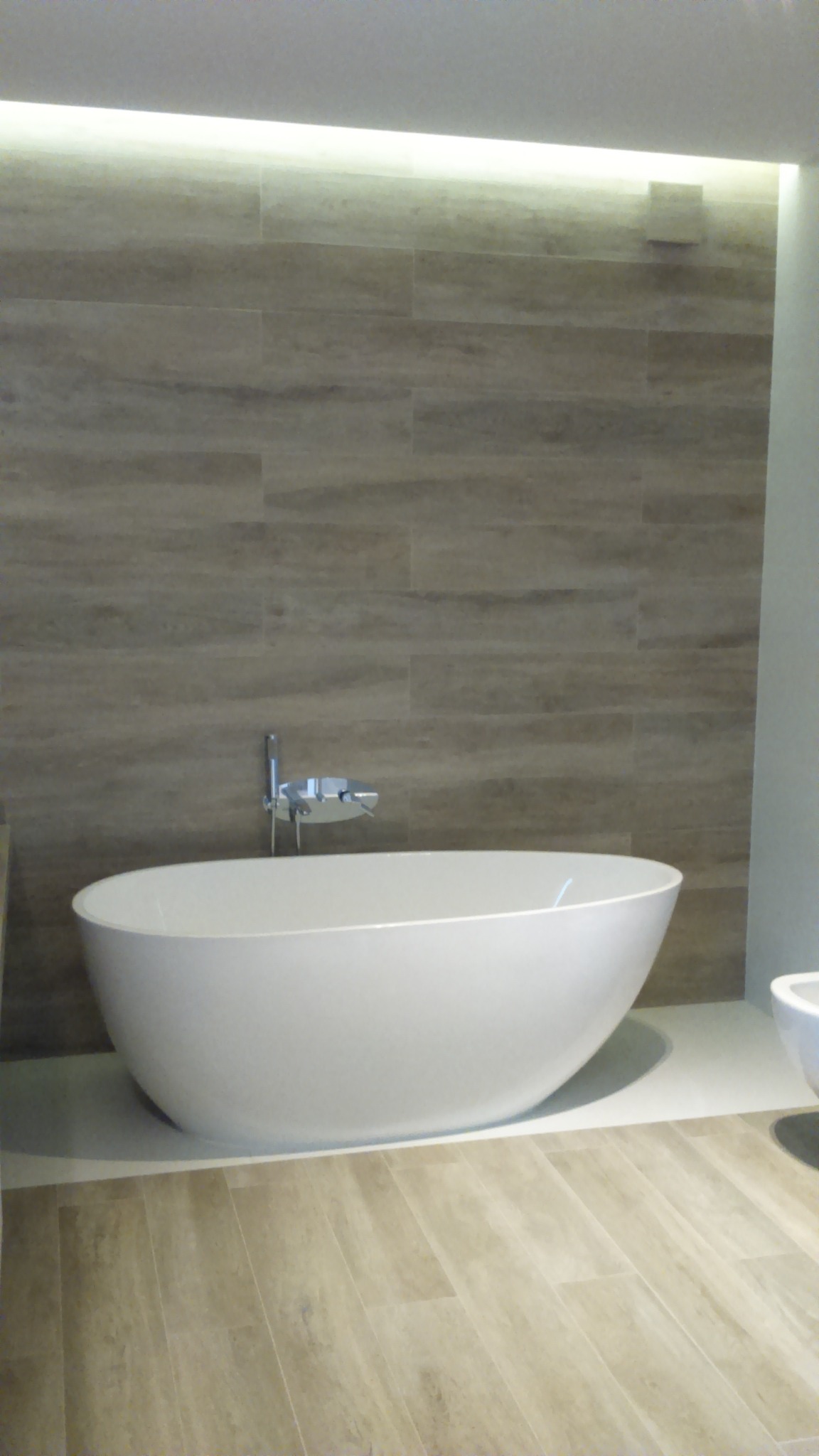 Nowoczesna łazienka z wolnostojącą wanną i płytkami imitującymi drewno na ścianie, oświetlona subtelnym światłem LED. Minimalistyczny design i eleganckie wykończenie.