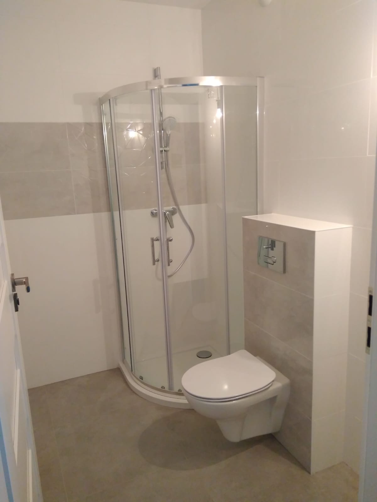 Nowoczesna kabina prysznicowa z hydromasażem i wisząca toaleta w wykończonej łazience z szarymi płytkami.