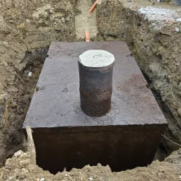 Wykop pod fundamenty z betonową studzienką inspekcyjną pośrodku, widoczna rura kanalizacyjna i fragment muru z bloczków.