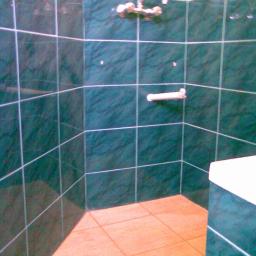 Sak-Bud - Wykończona kabina prysznicowa z ciemnozielonymi płytkami imitującymi marmur i jasną fugą. Na ścianie bateria i uchwyt na ręcznik. Na podłodze jasne, kwadratowe płytki.