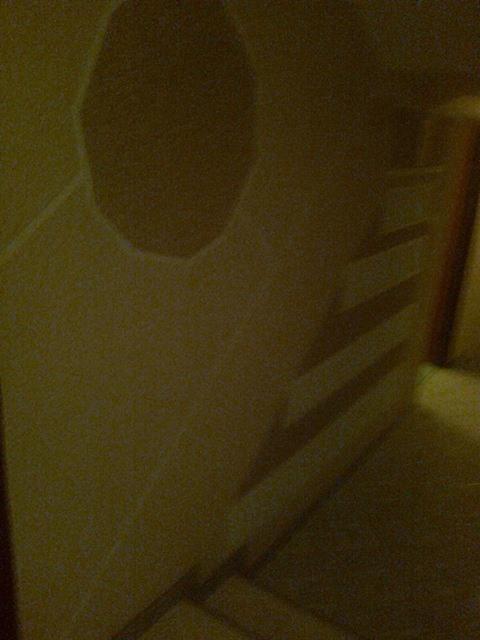 Niedokończona ściana z wyciętym otworem, przygotowana do dalszych prac wykończeniowych. Widoczne listwy dekoracyjne i surowe tło.