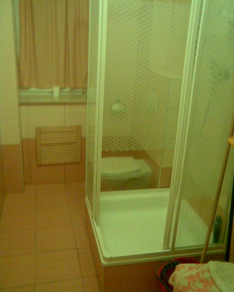 Wykończona łazienka z kabiną prysznicową z przezroczystymi drzwiami, brązowymi płytkami i drewnianym grzejnikiem drabinkowym. Widok na toaletę.