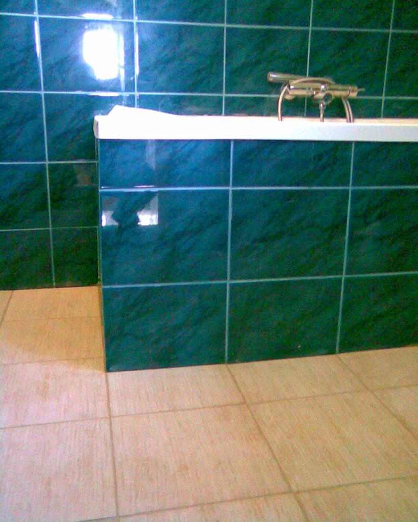 Wykończona łazienka z zielonymi płytkami ściennymi i beżowymi podłogowymi. Widoczna bateria wannowa i fragment wanny. Ukończony remont łazienki.