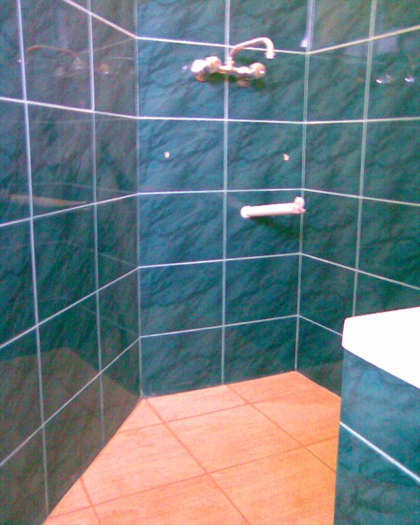 Wykończona kabina prysznicowa z ciemnozielonymi płytkami imitującymi marmur i jasną fugą. Na ścianie bateria i uchwyt na ręcznik. Na podłodze jasne, kwadratowe płytki.