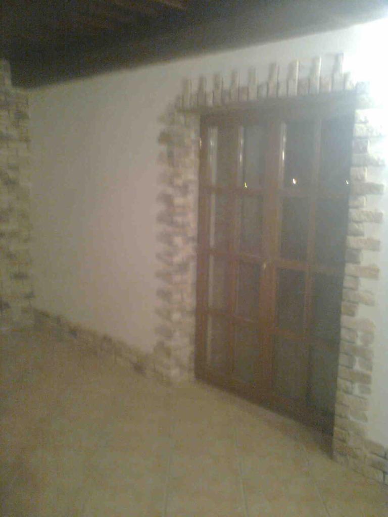 Wykończenie ściany przy drzwiach imitacją kamienia w odcieniach beżu i brązu. Dekoracyjne obramowanie wokół ościeżnicy. Jasna podłoga z płytek.