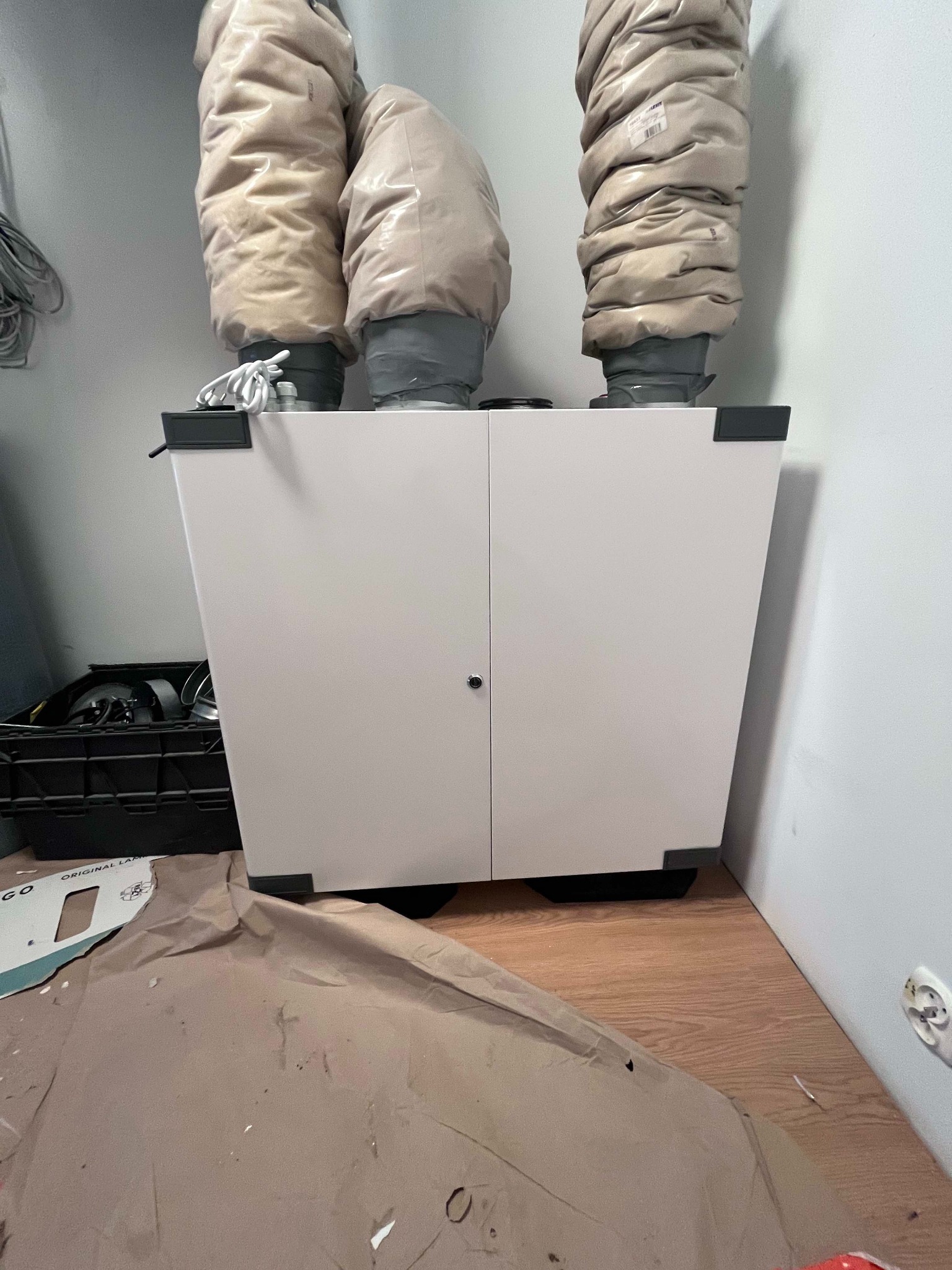 Biała jednostka centralna systemu wentylacji mechanicznej z trzema izolowanymi przewodami w Redzie, widoczna na podłodze kartonowa ochrona podczas montażu.