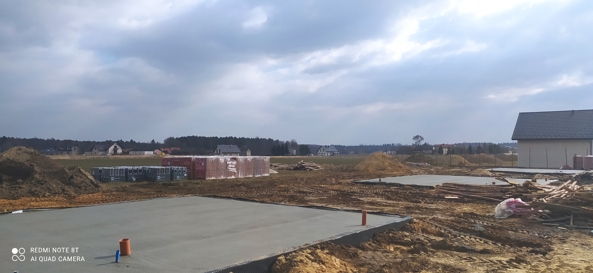 Wylane fundamenty pod budowę domu jednorodzinnego, widoczne bloczki fundamentowe, teren przygotowany pod dalsze prace, w tle zabudowa wiejska.