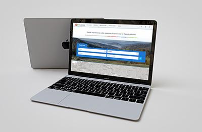 Laptop MacBook wyświetlający stronę internetową z formularzem wyszukiwania noclegów z motywem górskim w tle, prawdopodobnie z Małopolski, na białym tle.